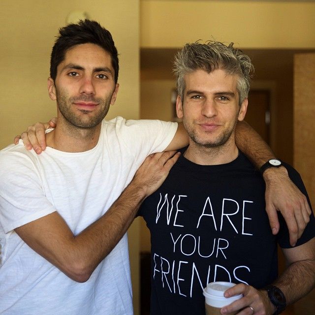 two men standing next to each other with one holding the other's arm around his shoulder