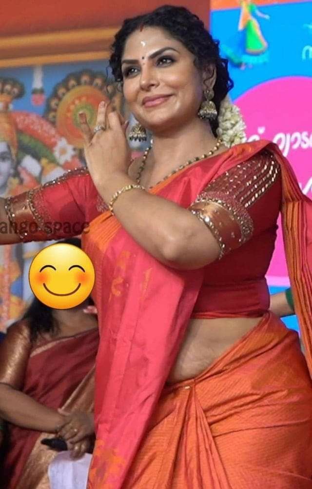 a woman in an orange and red sari dancing with a smile on her face