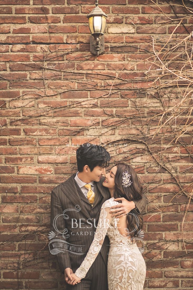 a man and woman standing next to each other in front of a brick wall