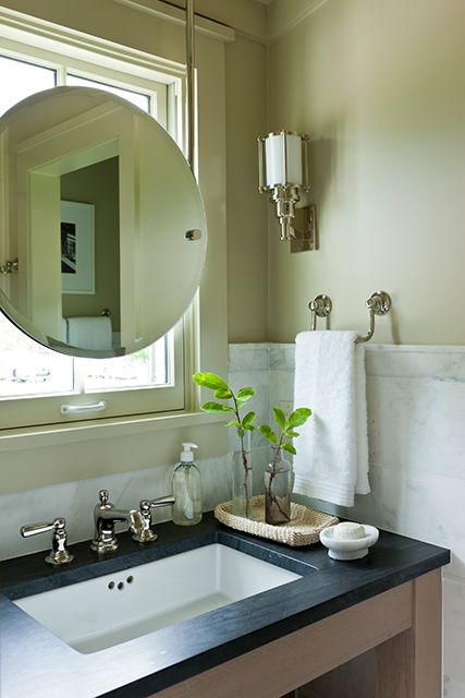 a bathroom sink sitting under a mirror next to a window with a potted plant in it