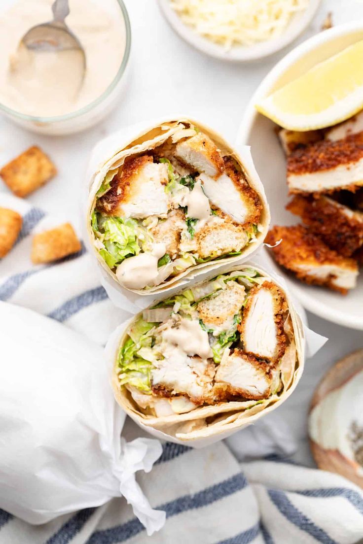 two wraps filled with chicken, lettuce and sauce on top of a table