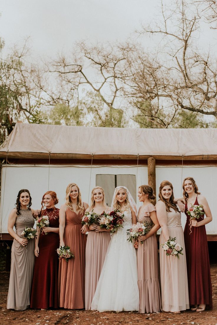 a group of women standing next to each other in front of a white tent with trees