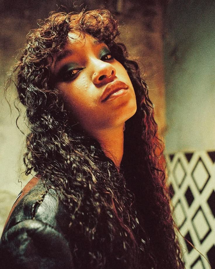 a woman with long curly hair and blue eyeshadow looking off into the distance