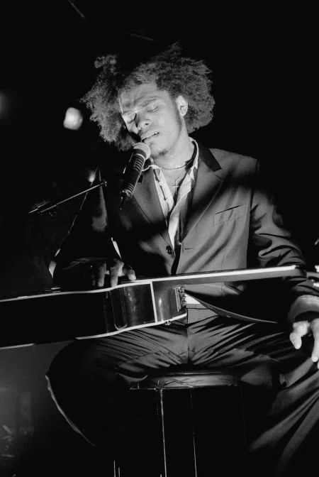 a man with curly hair sitting in front of a microphone and playing an instrument on stage