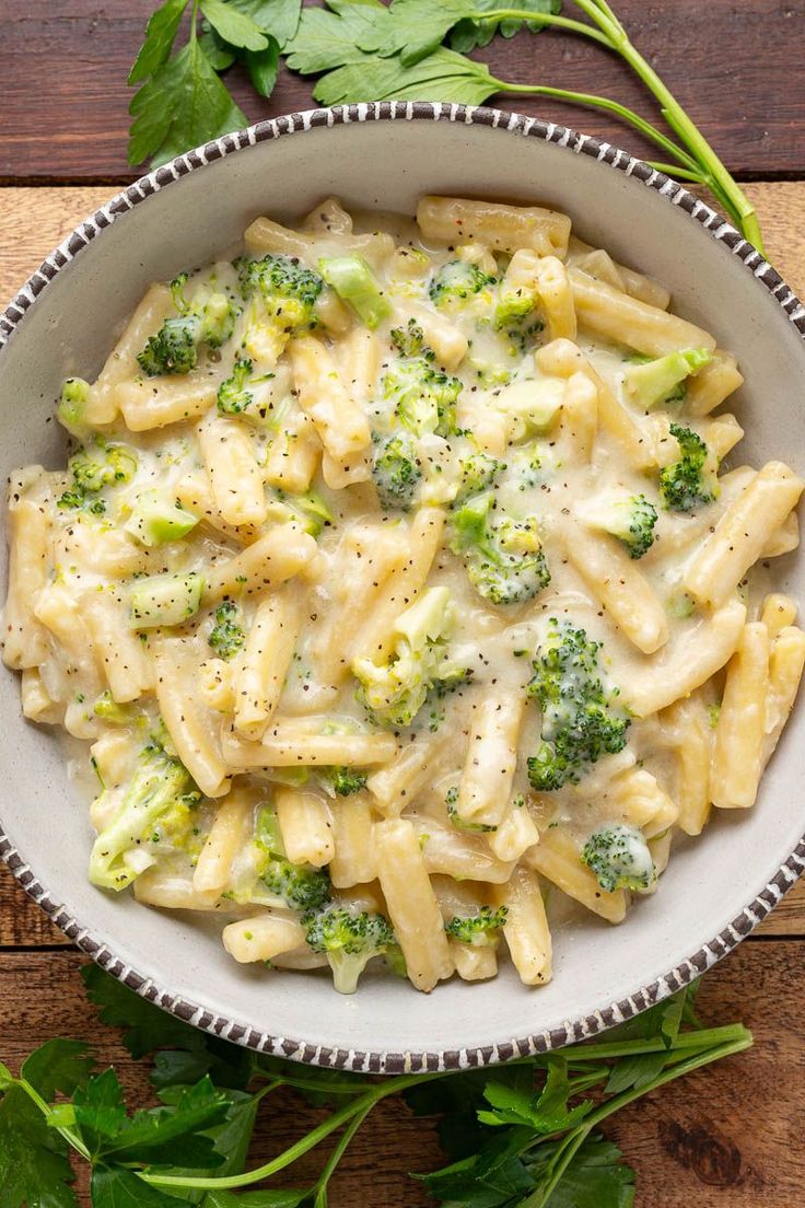 a white bowl filled with pasta and broccoli on top of a wooden table