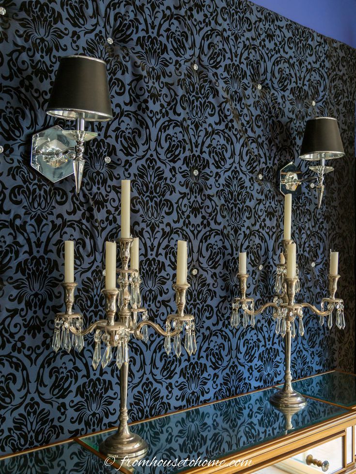 four candles are lit on a table in front of a wall with blue damask