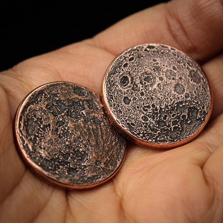 two small pieces of metal that are in someone's hand, one has the moon on it