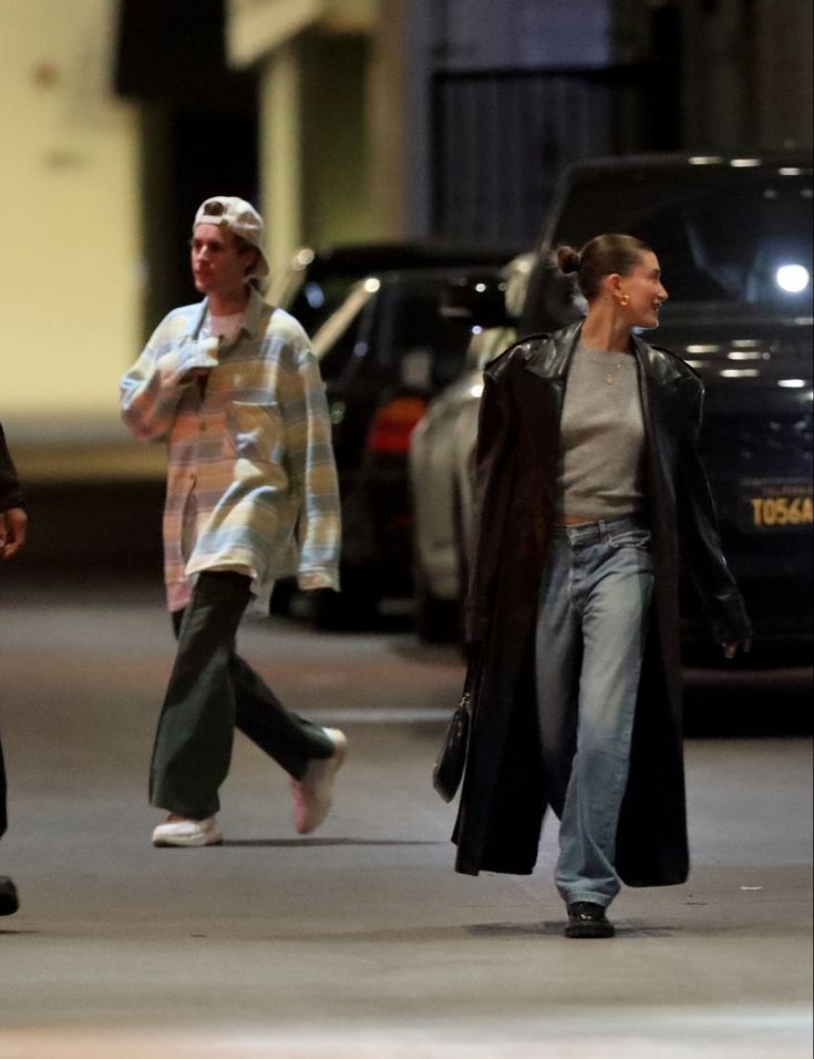 two people walking down the street with cars behind them