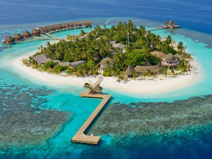 an island in the middle of some water with houses on it and palm trees around