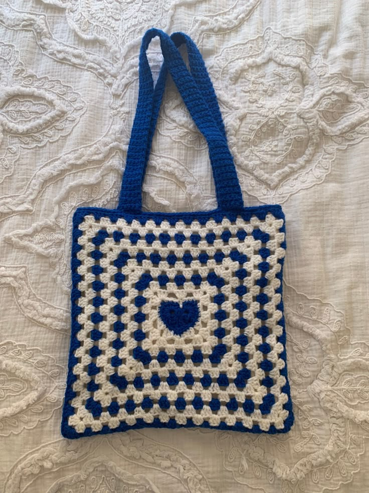 a crocheted blue and white bag with a heart in the center on a bed