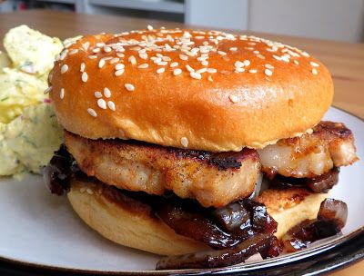 a hamburger with meat, onions and sauce on a plate next to a potato salad