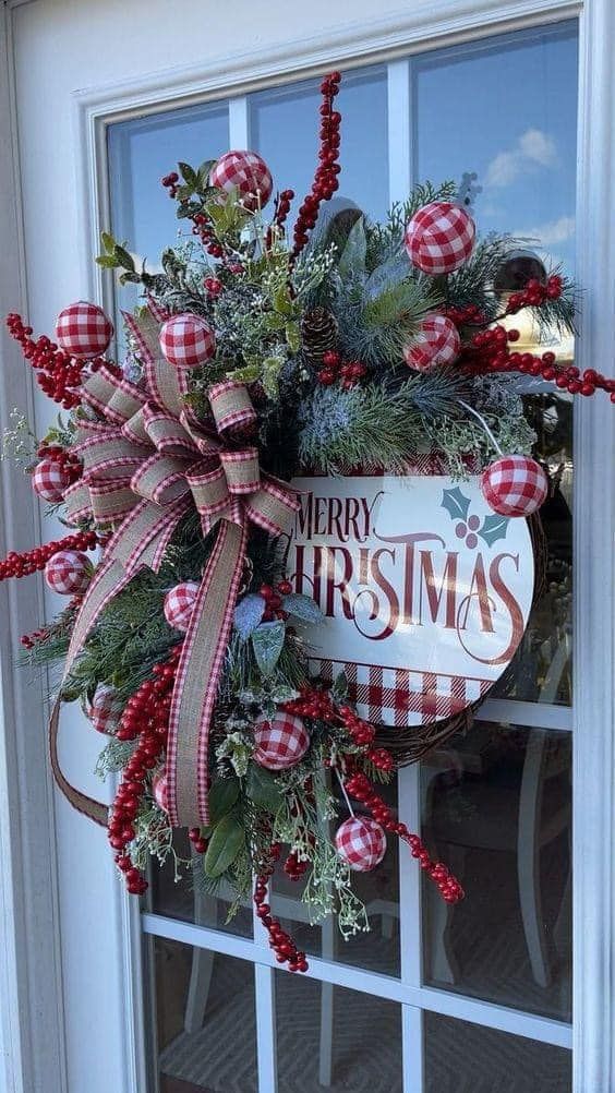 a christmas wreath is hanging on the front door with red and white plaid ribbon around it