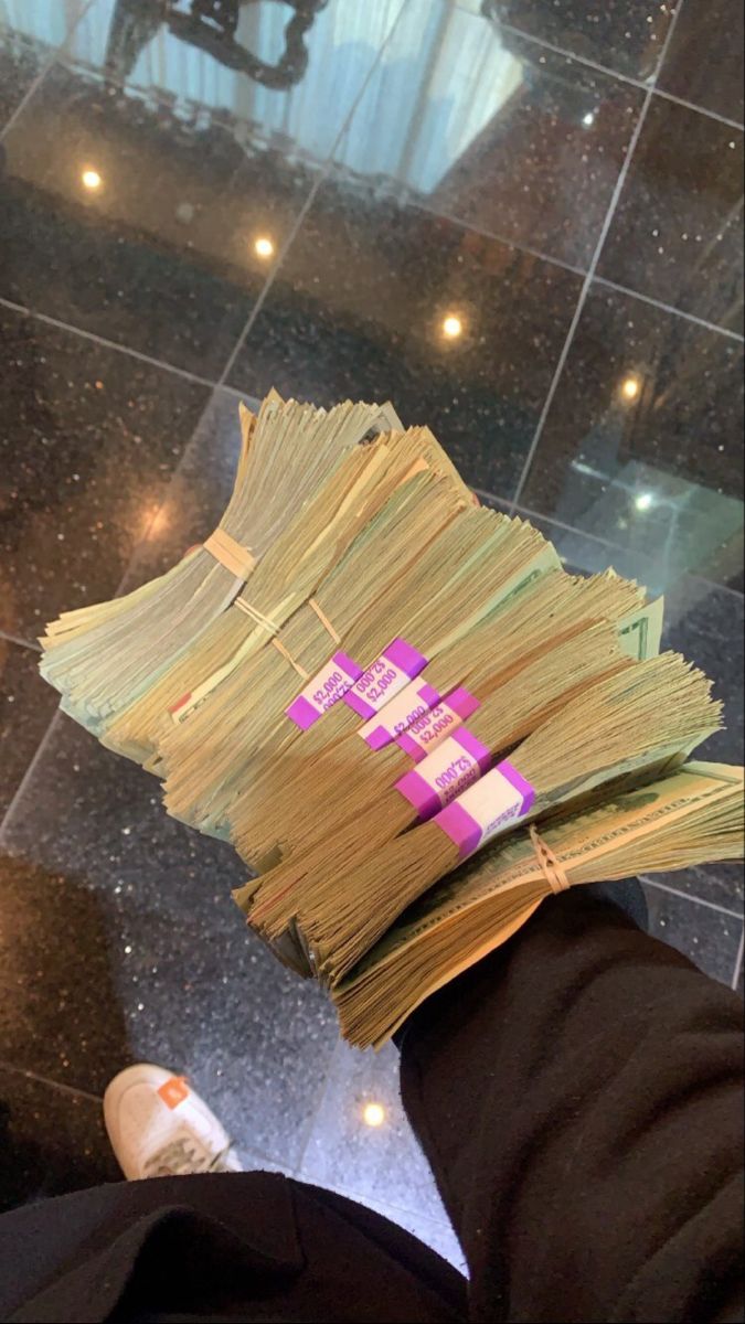 a stack of money sitting on top of a person's leg in front of a tiled floor