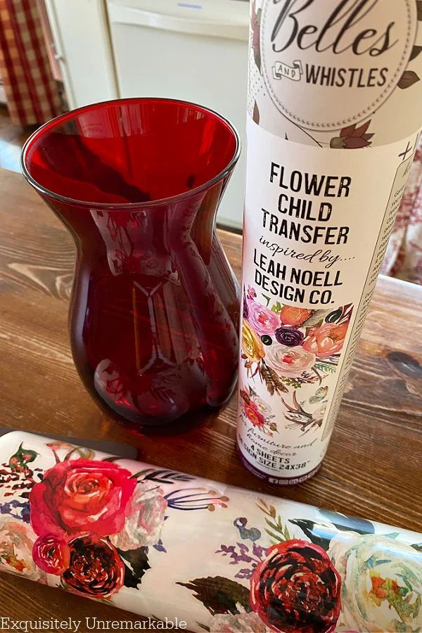 a red vase sitting next to a bottle of flower child transferer on top of a wooden table