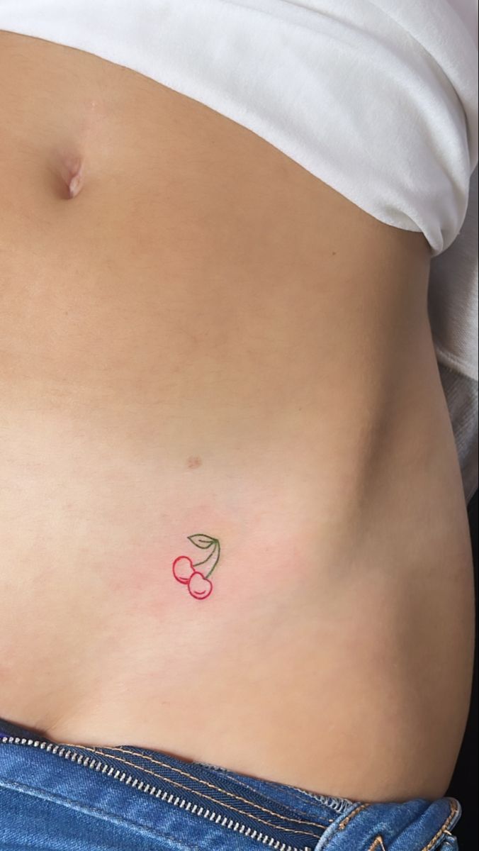 a woman's stomach with a small cherry tattoo on it