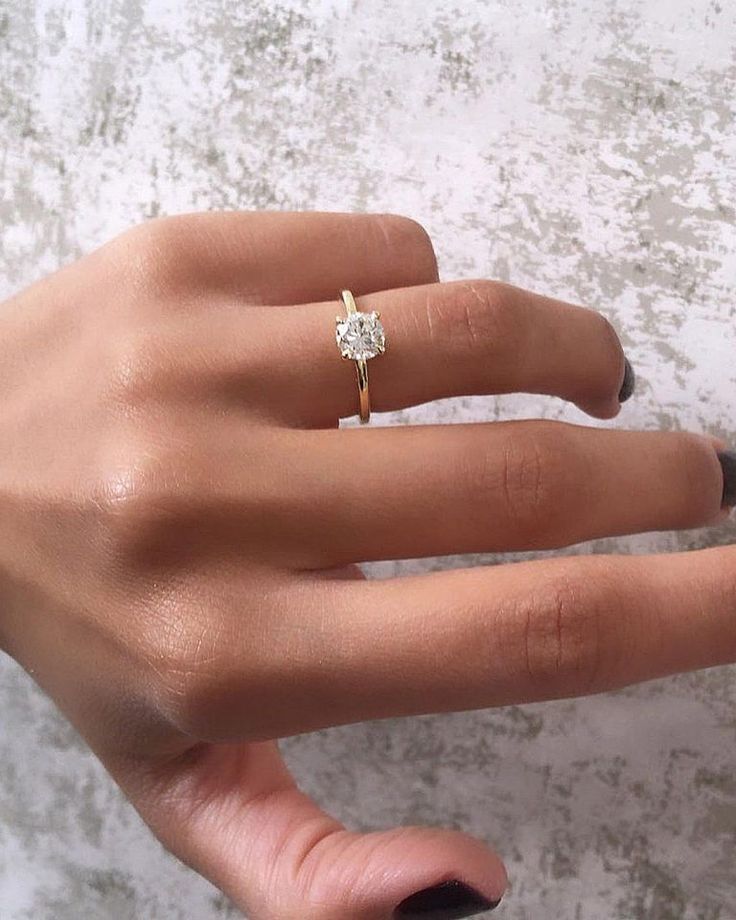 a woman's hand with a diamond ring on top of her finger, next to a wall