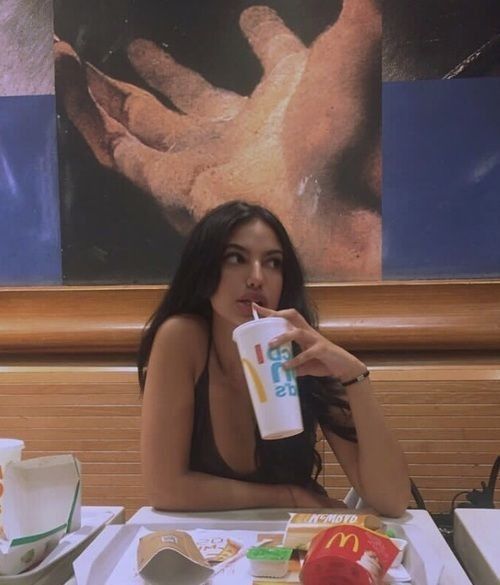 a woman sitting at a table eating and drinking from a cup with her mouth open