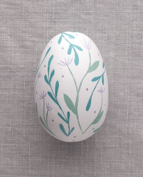 an egg decorated with flowers and leaves on a gray background, sitting on a linen surface