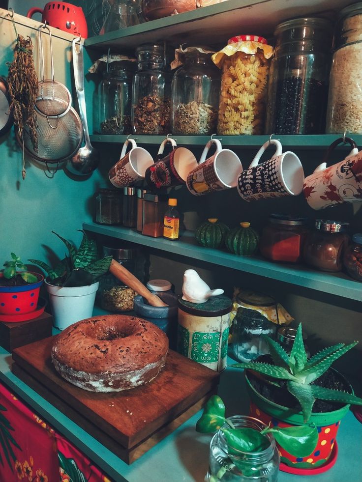 a shelf filled with lots of pots and pans next to a cake on top of a wooden cutting board