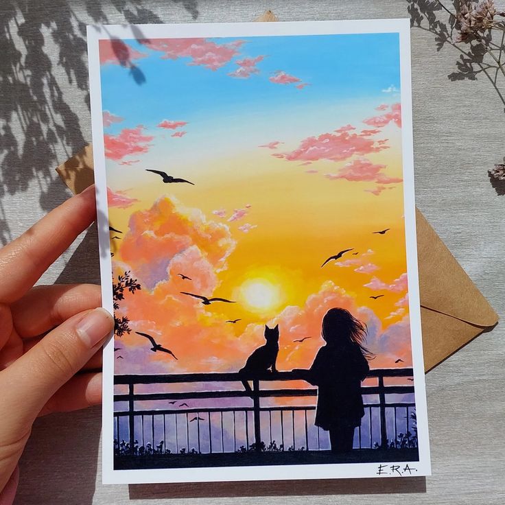 a person holding up a card with a painting of two cats on the fence and birds flying in the sky