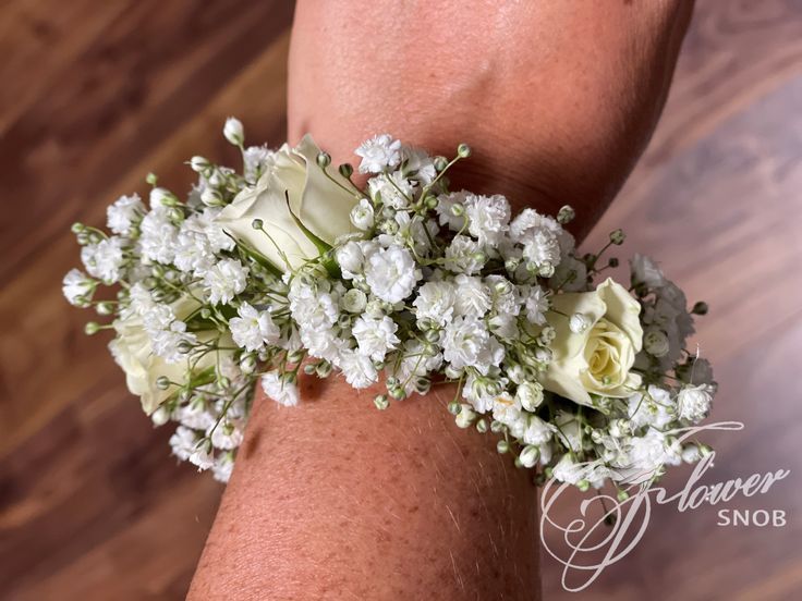 a woman's arm with white flowers and greenery on the wrist, close up