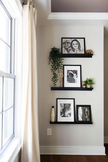 three black shelves with pictures and plants on them in front of a window, next to a white curtain