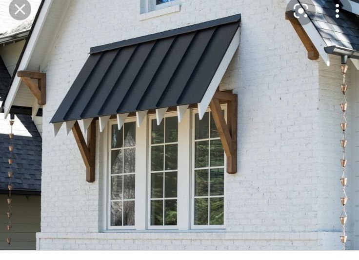 a white brick house with a black awning and wooden trim on the front window