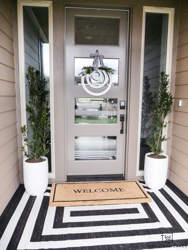 a welcome mat on the front door of a house with two potted plants next to it