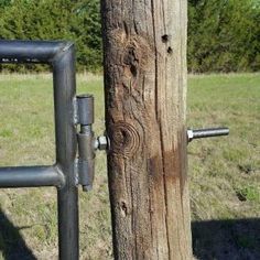 a wooden post with two metal bars attached to it, in front of a grassy field