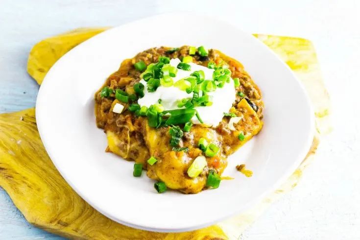 a white plate topped with taco covered in sour cream and green onion garnish