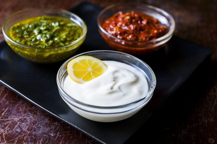 three bowls filled with different types of dips and sauces on a black tray