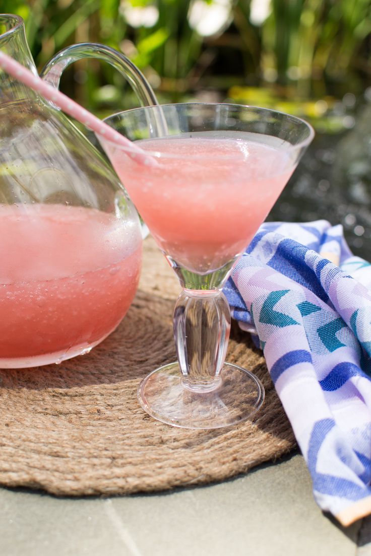 two glasses filled with pink liquid next to a pitcher and towel on a table outside