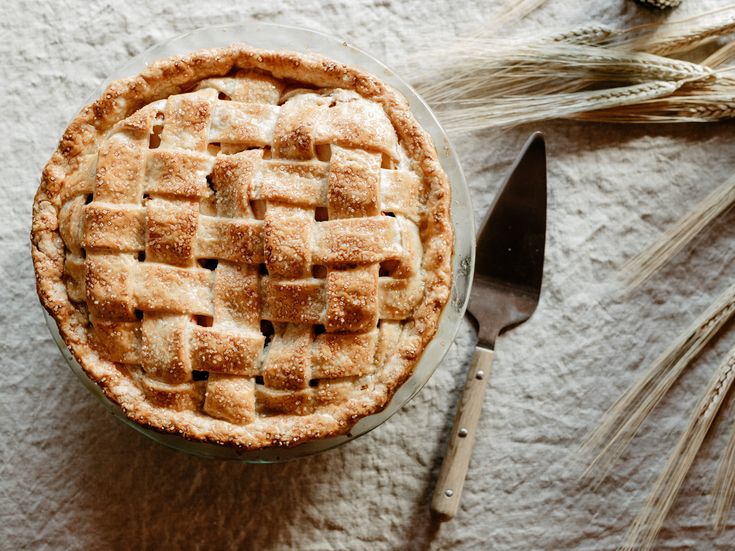 a pie sitting on top of a white table next to a fork and some ears of wheat