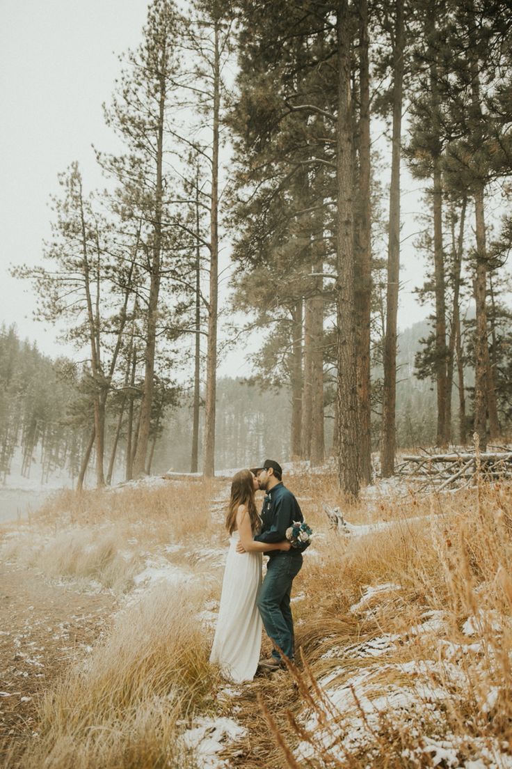 a bride and groom kissing in the snow surrounded by tall pine trees on their wedding day