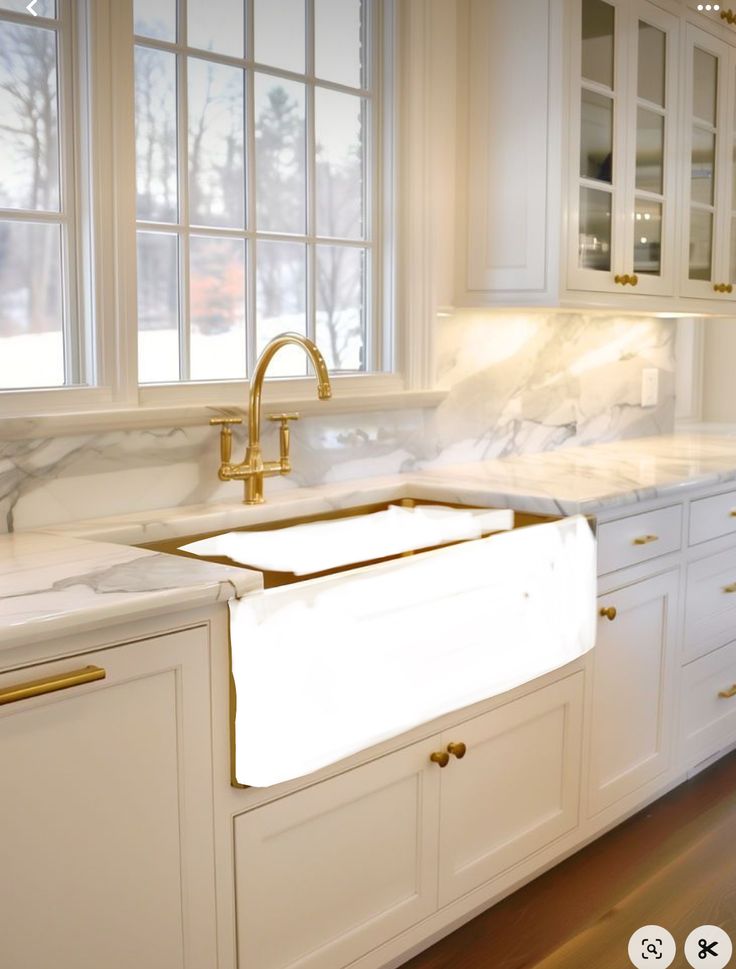 a white kitchen with marble counter tops and gold faucets on the windowsill