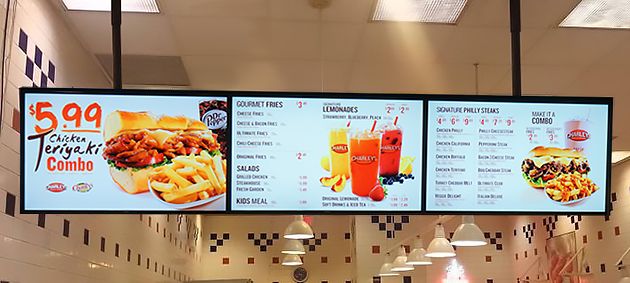 two large menus hanging from the ceiling in a fast food restaurant with checkered flooring