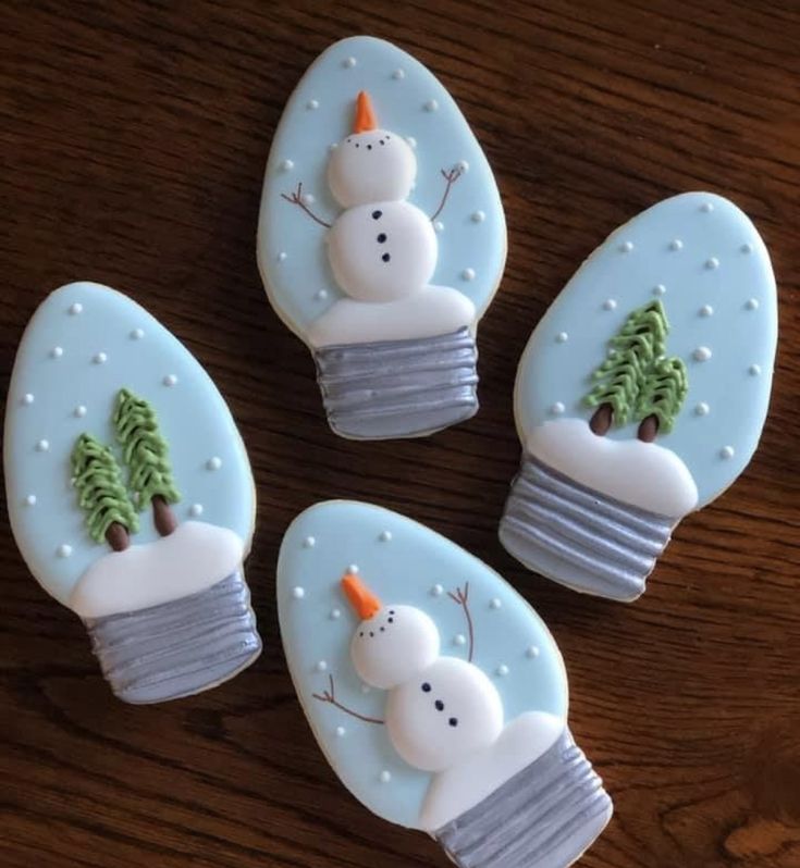 four decorated cookies with frosting and trees in them on top of a wooden table