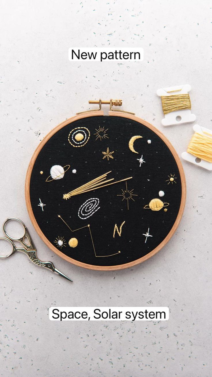 an embroidery project with space, stars and planets on the black surface next to scissors