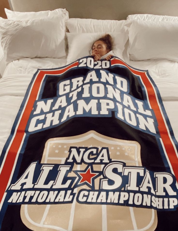 a woman laying in bed under a national championship blanket with the nca all star logo on it