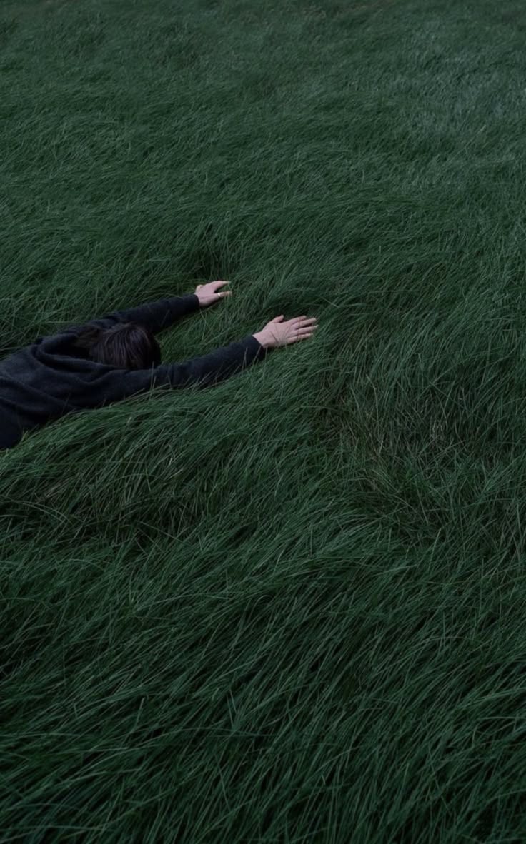 a person laying in the grass with their arms out and hands outstretched to reach for something