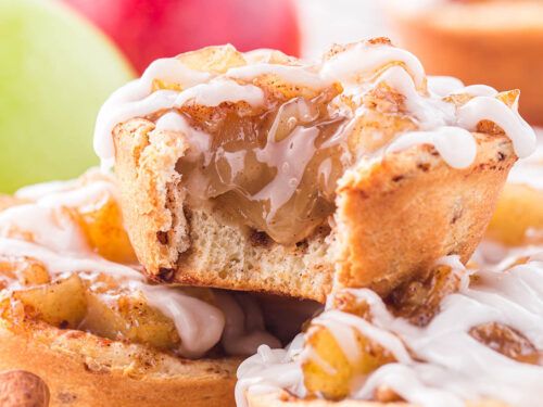 a muffin with white icing and nuts on it sitting next to an apple