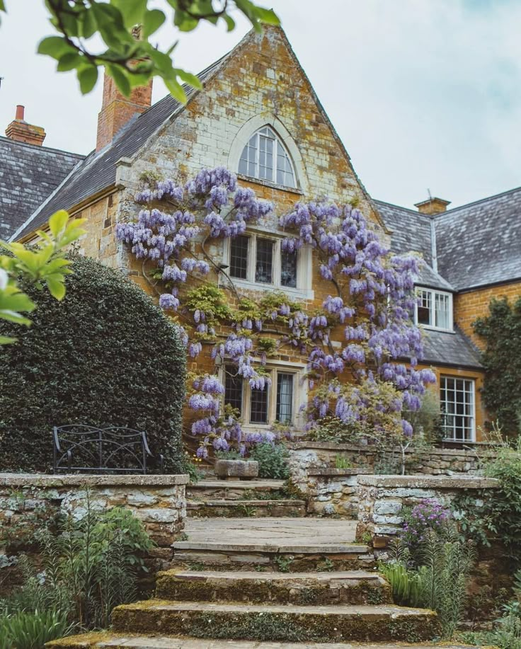 a stone house with purple flowers growing on it's walls and steps leading up to the front door