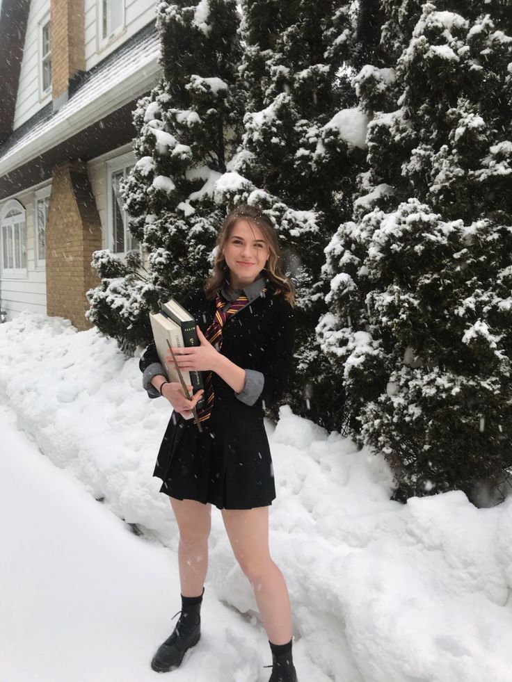 a woman standing in the snow holding an open book and looking at the camera while wearing black boots