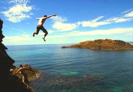 a man jumping off the edge of a cliff into the ocean with his feet in the air