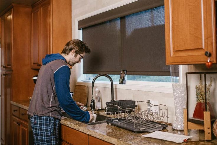 a young man is washing dishes in the kitchen with his hands on the sink drainer