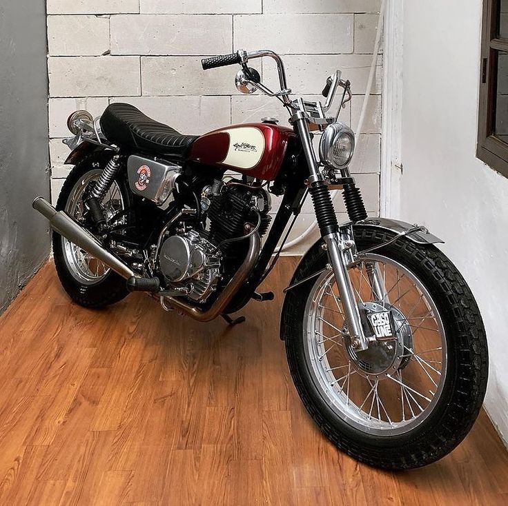 a red and black motorcycle sitting on top of a wooden floor next to a brick wall