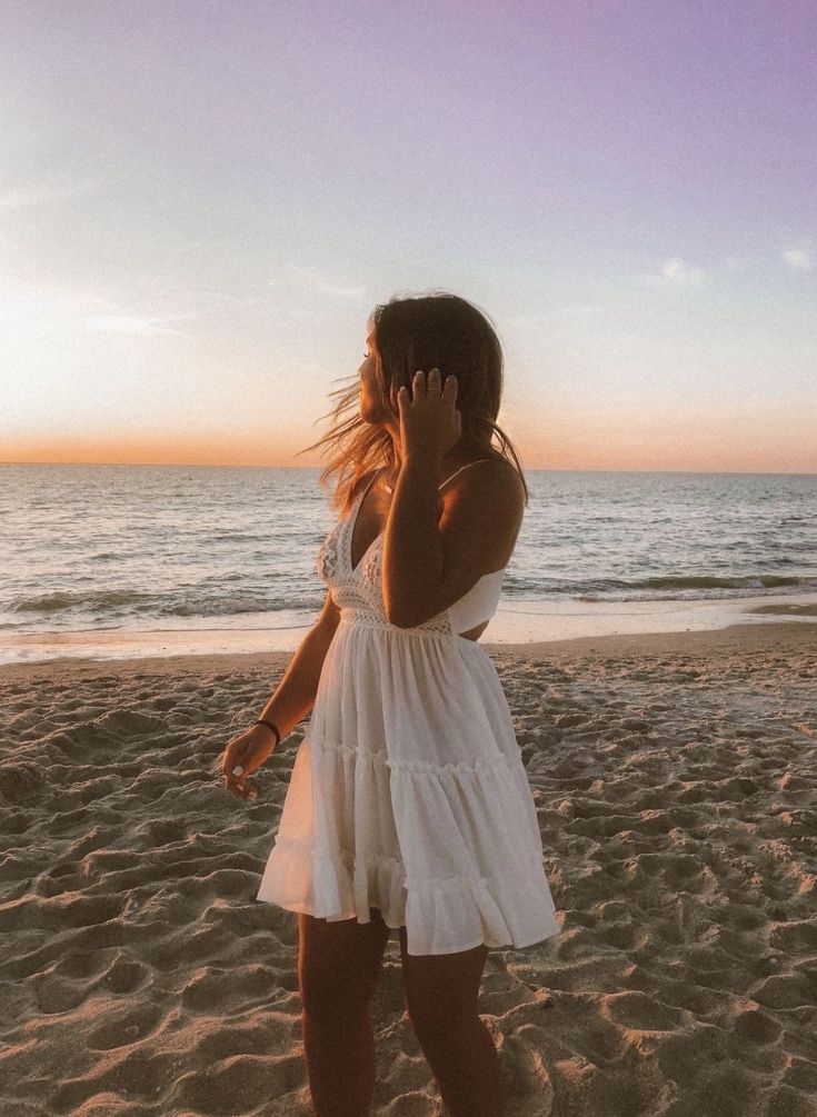 a woman standing on top of a beach next to the ocean talking on a cell phone