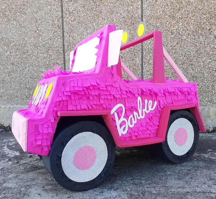 a pink toy truck with barbie written on the front and back tires, parked in front of a wall