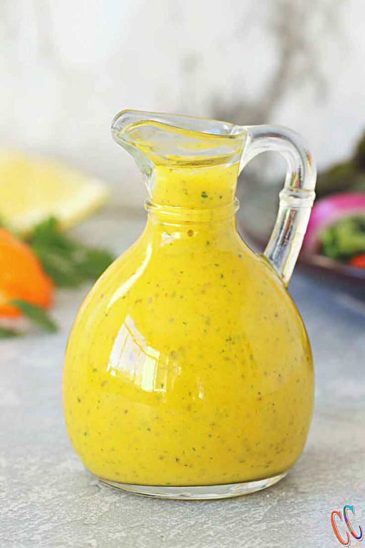 a glass pitcher filled with yellow liquid sitting on top of a counter next to vegetables