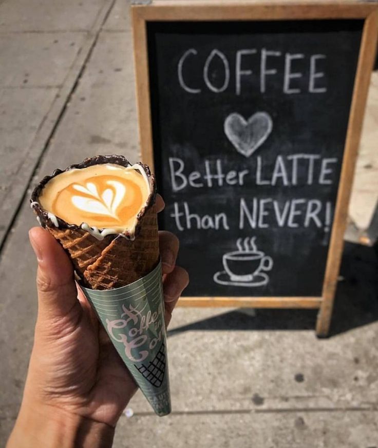 a hand holding an ice cream cone with coffee on it next to a chalkboard sign